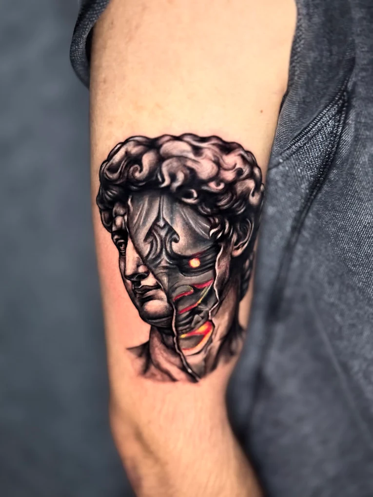 Black and grey David statue tattoo cracking open with fire inside and colour accent, upper arm, by Joseph Bsaibess